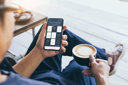   Sedící muž s šálkem kávy v jedné ruce a smartphonem v druhé. Na obrazovce je vidět aplikace TaHoma.