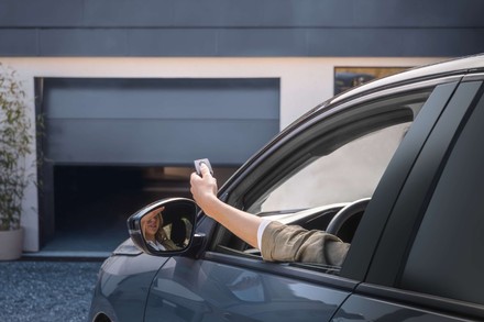  Žena sedící v autě otevírá automatickou garážová vrata pomocí dálkového ovladače.
