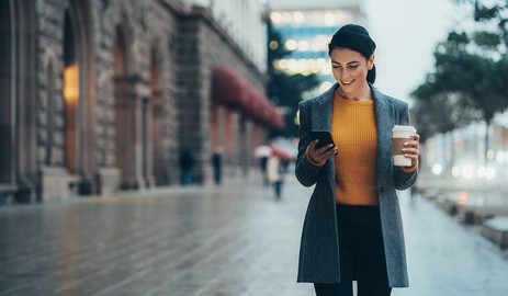 somfy-woman-walking-street-smartphone-coffee